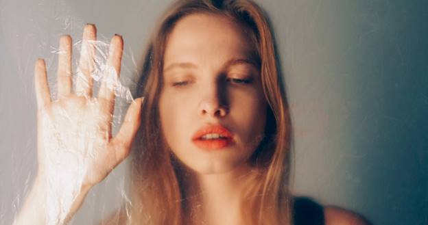 A person presses their hand against plastic. With eyes closed and red lipstick, the person is featured in a blog post about revenge porn.